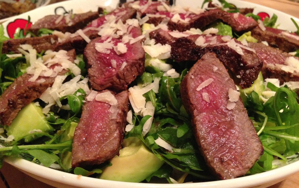 Ein saftiges Steak auf einem Bett aus Rucola mit cremiger Avocado und Parmesan