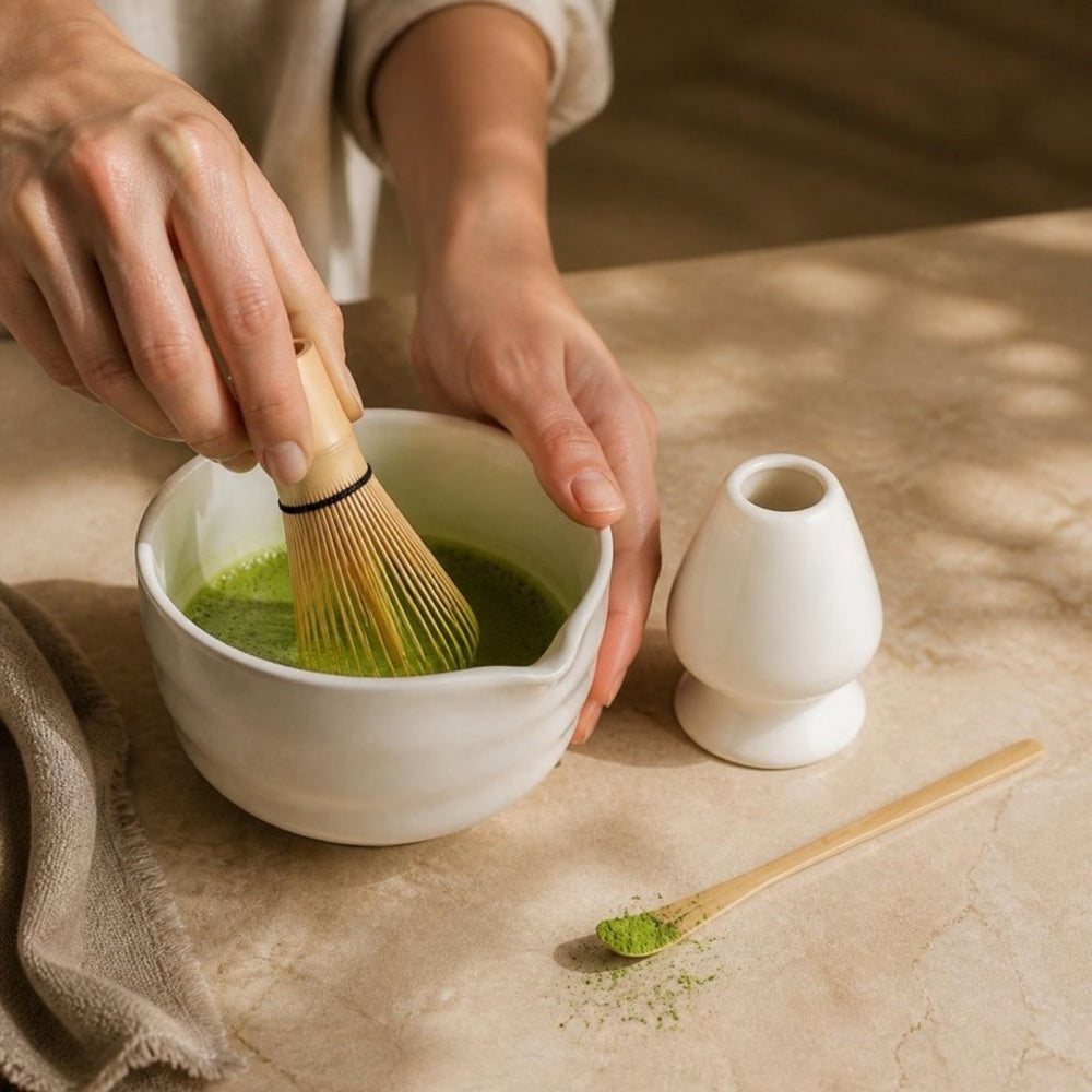 Handen kloppen matcha met de bamboe garde in de witte matchakom