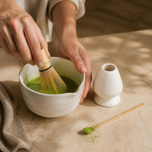 Handen kloppen matcha met de bamboe garde in de witte matchakom