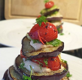 Ein farbenfroher Turm aus gegrillter Aubergine mit Avocado, Hummus und Kirschtomaten